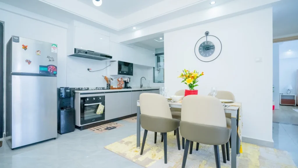Fitted kitchen with stainless steel cooktop, oven, refrigerator, and dining setup at Orchid Residency Westlands