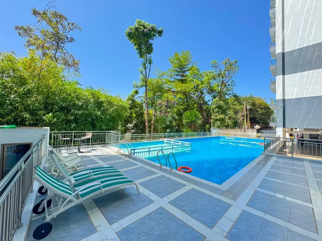 Outdoor swimming pool deck with sun lounger chairs surrounded by trees at Orchid Residency Westland