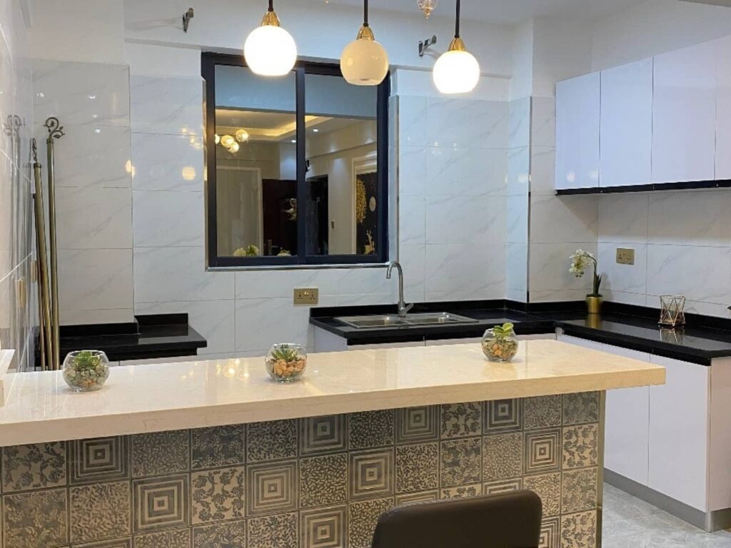 Modern fitted kitchen featuring white cabinetry, black granite countertops, patterned tile breakfast bar counter, and pendant lights at Diamond Homes in Kileleshwa, Nairobi.