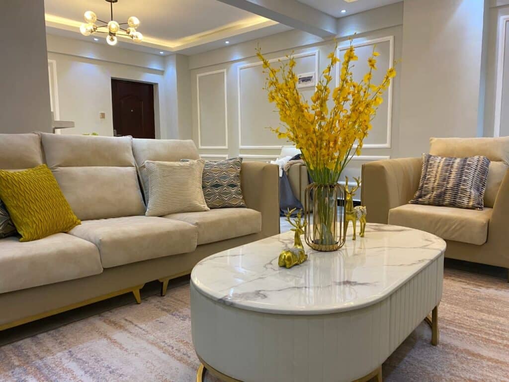 Spacious and luxurious living room lounge featuring neutral-toned sectional seating, marble coffee table, and floral centerpiece at Diamond Homes in Kileleshwa, Nairobi.
