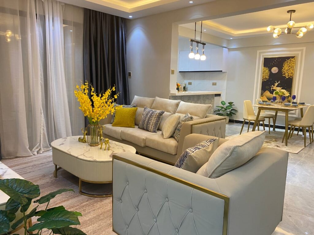 Open-plan living room and dining area with large windows, sheer curtains, and warm ambient lighting at Diamond Homes in Kileleshwa, Nairobi.