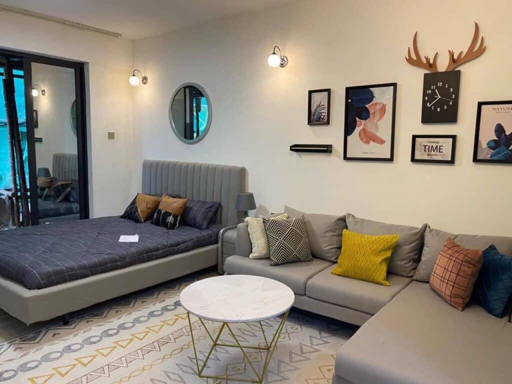 Combined studio apartment bedroom and cozy lounge area with sectional sofa, upholstered bed, and patterned rug at Diamond Homes in Kileleshwa, Nairobi.