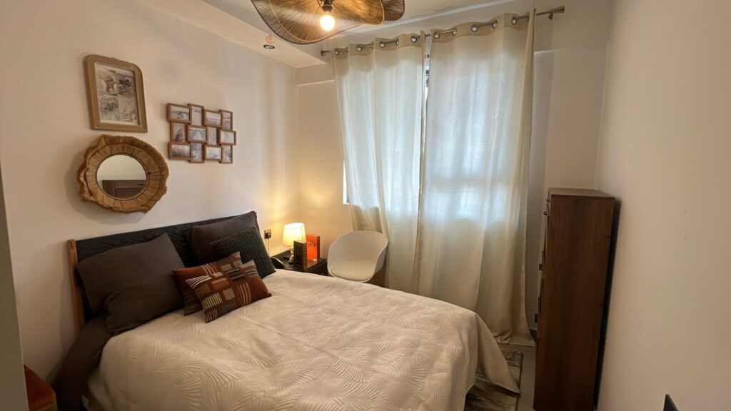 Cozy bedroom interior with double bed, bedside lamp, decorative round wall mirror, and natural curtain lighting at Serenity Residence in Kilimani, Nairobi.