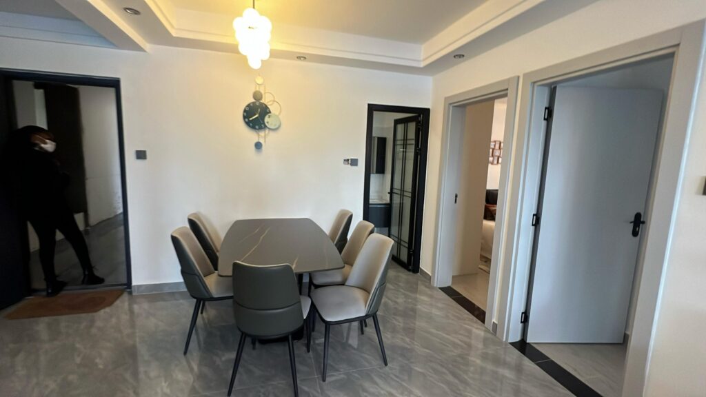 Modern dining space featuring a 6-seater dining table set with grey upholstered chairs and decorative wall clock at Serenity Residence in Kilimani, Nairobi.