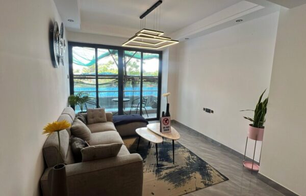 Contemporary living room lounge featuring grey sectional sofa, geometric pendant lighting, and sliding glass doors to the balcony at Serenity Residence in Kilimani, Nairobi.