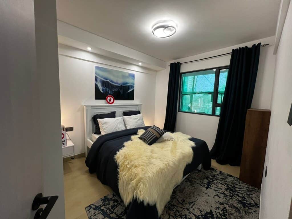Elegantly styled master bedroom with dark bedding, furry throw rug, wall art, and bedside lighting at Serenity Residence in Kilimani, Nairobi.
