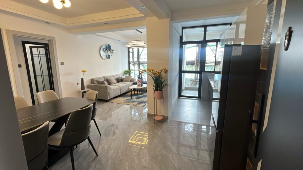 Wide-angle interior perspective looking across the open-plan dining and living space toward the kitchen at Serenity Residence in Kilimani, Nairobi.