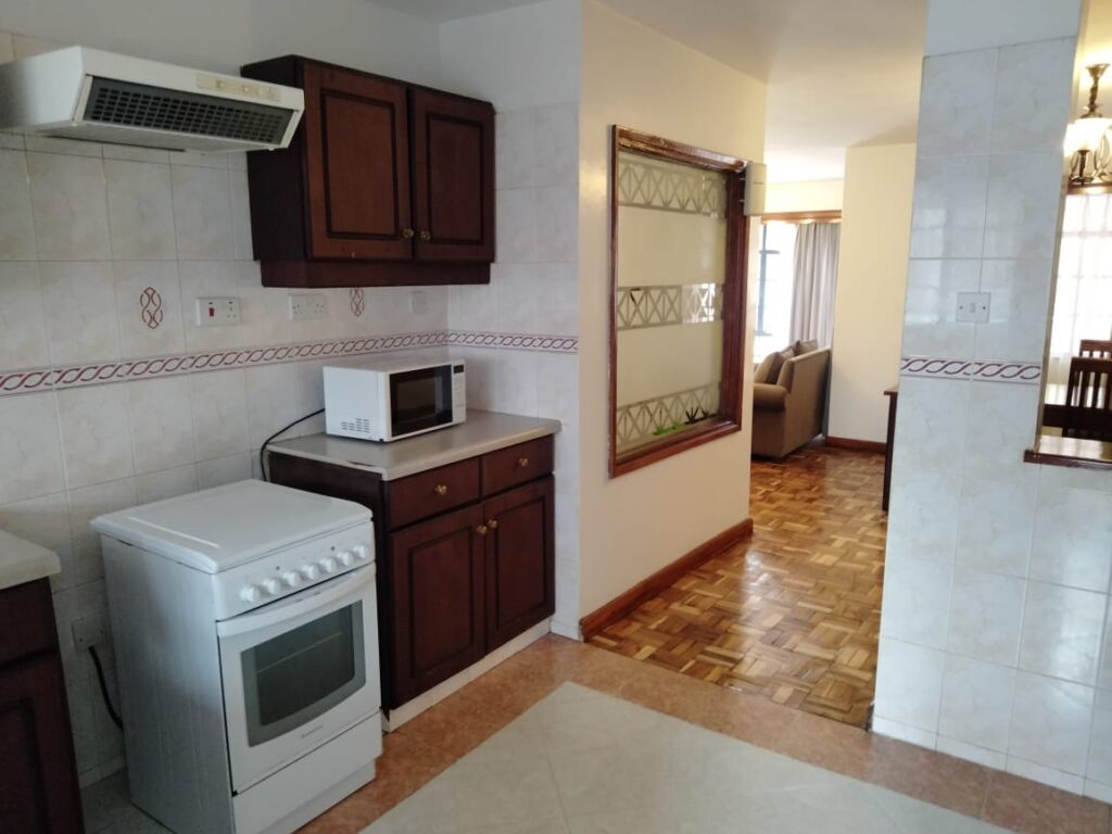 Fitted kitchen with dark wood cabinetry, cooker stove, and view into living area at Capital Apartments Valley Arcade