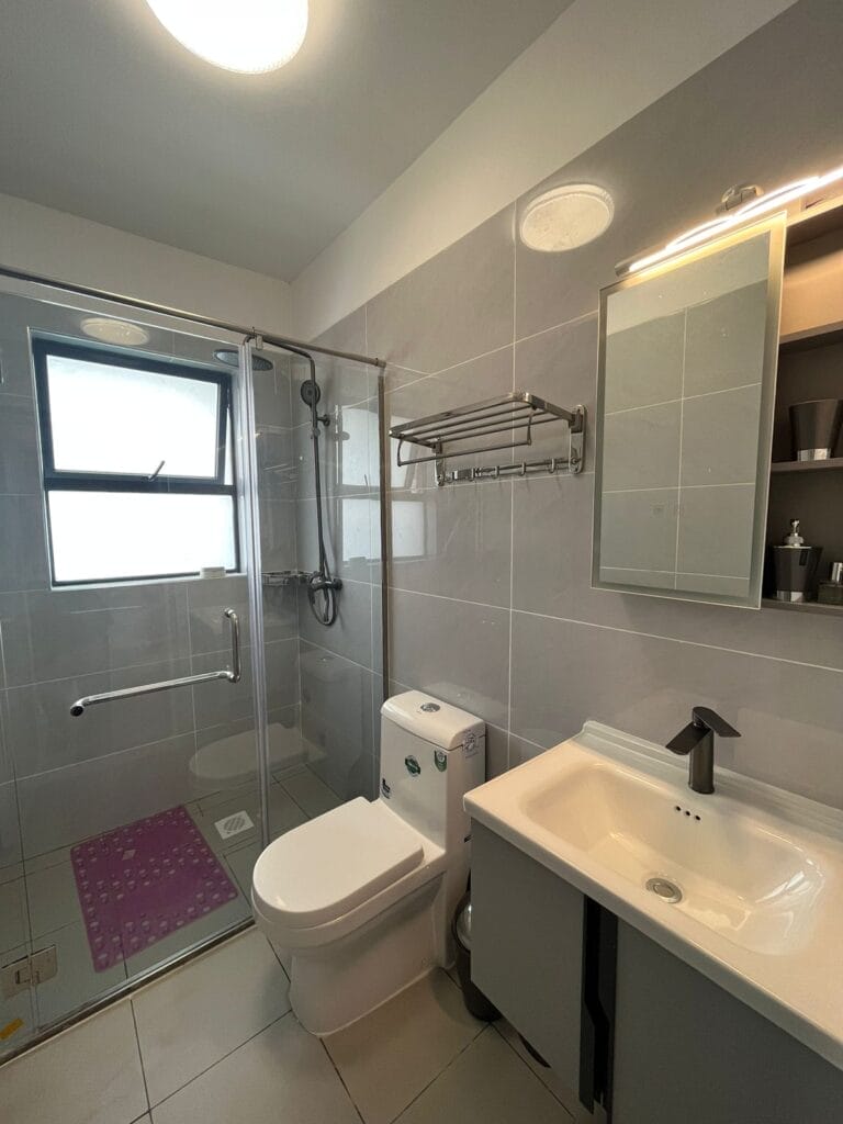 Contemporary bathroom featuring a glass walk-in shower enclosure, floating vanity, backlit mirror, and grey wall tiles at New Rise Gardens in Syokimau, Nairobi.