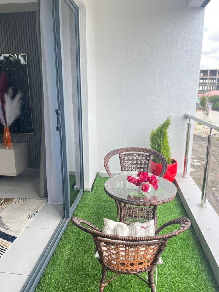 Private apartment balcony with artificial turf and outdoor coffee table set at New Rise Gardens in Syokimau, Nairobi.