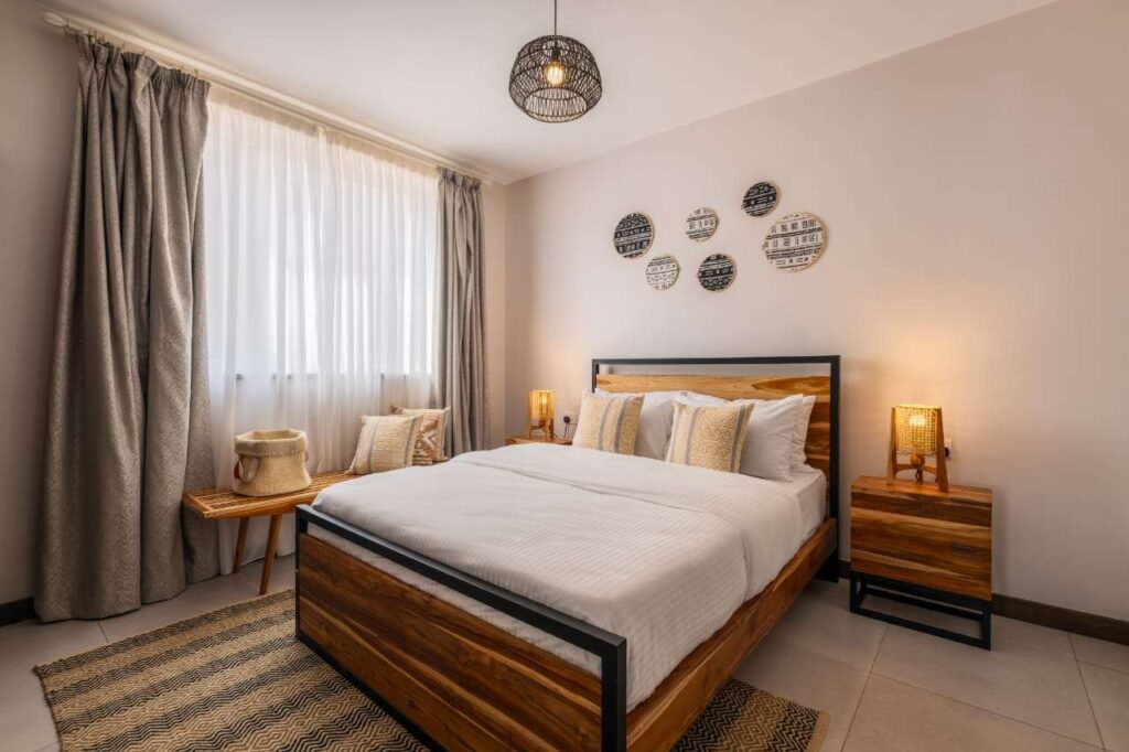Master bedroom interior featuring a solid wood bed frame, matching bedside tables, woven pendant lighting, and decorative wall art at Sunpark Residences in Syokimau, Nairobi.