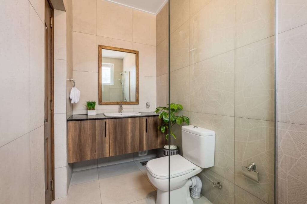Contemporary bathroom featuring a glass walk-in shower enclosure, wooden floating vanity, framed mirror, and cream wall tiles at Sunpark Residences in Syokimau, Nairobi.